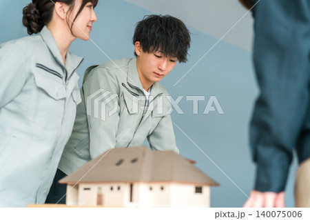 住宅模型を使って会議・ミーティング・打ち合わせ作業服姿の建設業・建築業の男女のビジネスマン 住宅模型を使って会議・ミーティング・打ち合わせ作業服姿の建設業・建築業の男女のビジネスマン 140075006