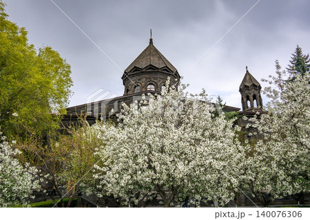 White flowering cherry trees frame old stone church under gray sky 140076306