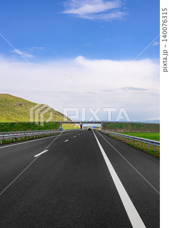 Empty highway leads to bridge over horizon with rolling hills in background Empty highway leads to bridge over horizon with rolling hills in background 140076315