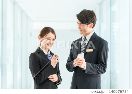 スマホを持って会話するビジネスマンとビジネスウーマン(ホテルマン,コンシェルジュ,CA)) スマホを持って会話するビジネスマンとビジネスウーマン(ホテルマン,コンシェルジュ,CA)) 140076724