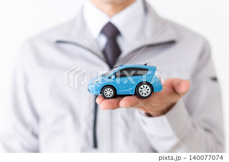 自動車の模型を持つグレーの作業着姿のミドル男性ビジネスマン白バック 140077074