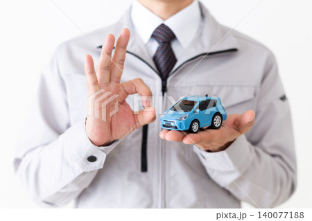 自動車の模型を持って丸のポーズをするグレーの作業着姿のミドル男性ビジネスマン白バック 140077188