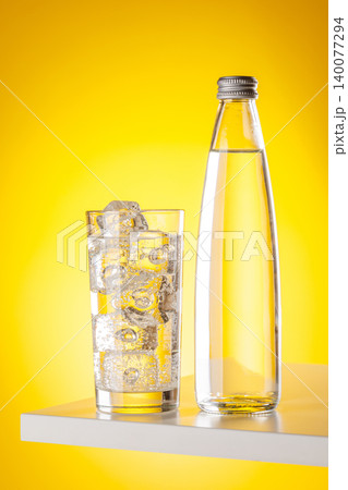 Glass of sparkling water with ice cubes on yellow background minimal Glass of sparkling water with ice cubes on yellow background minimal 140077294