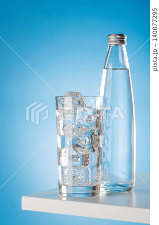 Glass of sparkling water with ice cubes on blue background minimal Glass of sparkling water with ice cubes on blue background minimal 140077295