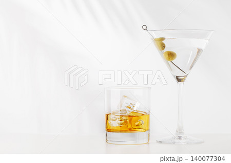 Glass of whiskey with ice and martini with olives on white background 140077304