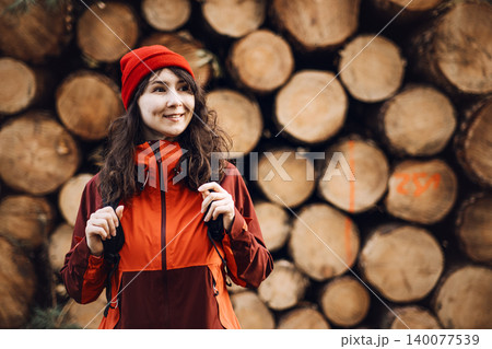 Smiling woman stands in front of stacked timber logs in woodland area. Woman forest inspector, female industrial professional, environmental auditor at work. 140077539