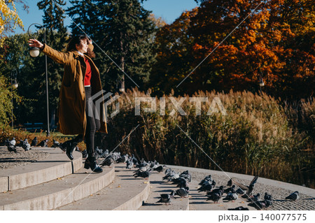 Woman moves joyfully with outstretched arms on stone steps in public park while pigeons gather nearby. Mindfulness in motion, radiant smile outdoor, cheerful emotional expression. Woman moves joyfully with outstretched arms on stone steps in public park while pigeons gather nearby. Mindfulness in motion, radiant smile outdoor, cheerful emotional expression. 140077575
