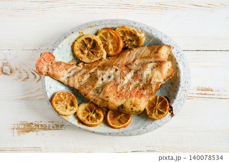 Grilled red snapper served on a white plate with lemon slices around the fish on a wooden table Grilled red snapper served on a white plate with lemon slices around the fish on a wooden table 140078534
