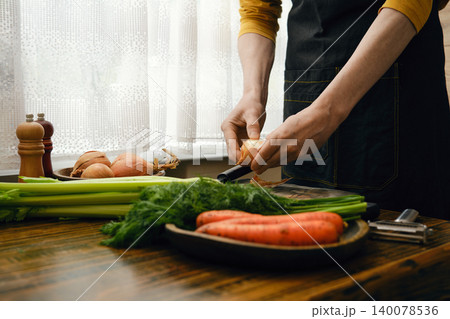 Person prepares vegetables in a kitchen during daylight for a meal Person prepares vegetables in a kitchen during daylight for a meal 140078536