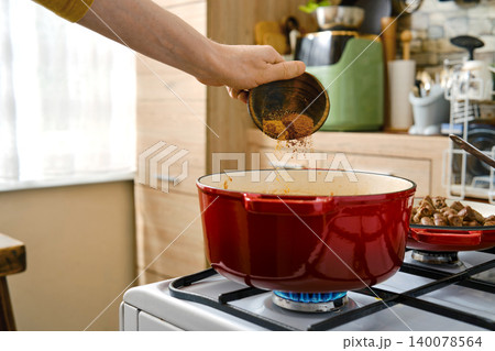 Person adds spices to pot on stove in kitchen during daytime cooking session Person adds spices to pot on stove in kitchen during daytime cooking session 140078564
