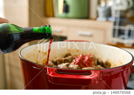 Cooking with red wine in a pot with meat and sauce during day time in a kitchen 140078566