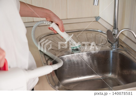 Cleaning a kitchen sink with a handheld steam cleaner during a home cleaning session 140078581