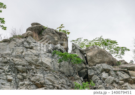 Rugged rocky cliff scattered green vegetation weathered boulders highlighting natural geology resilience outdoor landscape scenery Rugged rocky cliff scattered green vegetation weathered boulders highlighting natural geology resilience outdoor landscape scenery 140079451