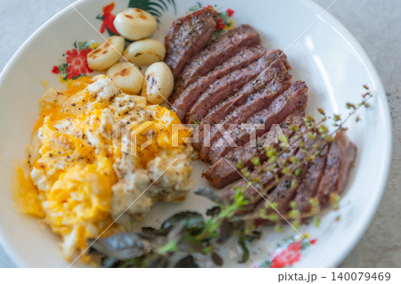 Juicy sliced steak served scrambled eggs roasted garlic fresh herbs Gourmet breakfast meal rich protein savory flavors 140079469