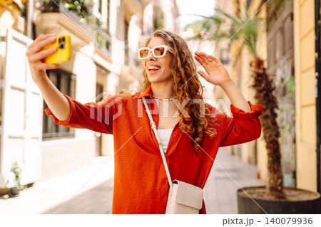 Cheerful woman taking a selfie in stylish sunglasses while strolling down a sunlit city street Cheerful woman taking a selfie in stylish sunglasses while strolling down a sunlit city street 140079936