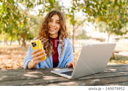 Happy woman with laptop and phone at table in an outdoor near lake. Business, blogging, freelancing. 140079952
