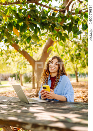 Happy woman with laptop and phone at table in an outdoor near lake. Business, blogging, freelancing. 140079954
