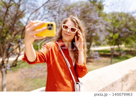 Young woman taking a cheerful selfie in blooming park on a sunny day. Joy concept. Active lifestyle. 140079963