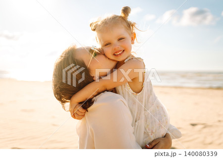 Portrait of mother and daughter enjoying a beach stroll at sunset. Moment of love and playfulness 140080339