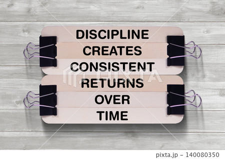 Discipline Creates Consistent Returns Over Time tagline written on wooden stick hold by binder clip with wooden texture background, business and investment, stock market theme 140080350
