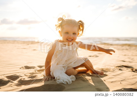 Little girl plays joyfully along the sandy beach during a sunny day by the ocean Little girl plays joyfully along the sandy beach during a sunny day by the ocean 140080382