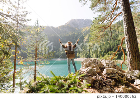 Back view young woman with backpack looking the view of the mountain lake in sunny weather. Back view young woman with backpack looking the view of the mountain lake in sunny weather. 140080562