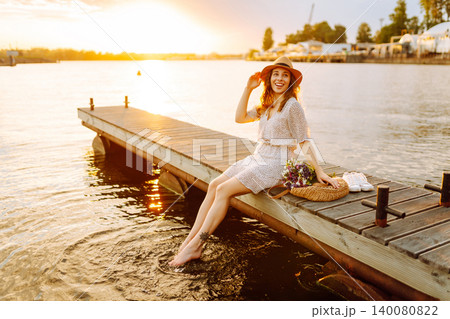 Young woman in dress sitting on wooden pier near pond. Rustic style of wedding. Travel, tourism Young woman in dress sitting on wooden pier near pond. Rustic style of wedding. Travel, tourism 140080822