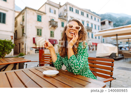 Happy woman sitting by table drinking coffee of outdoor sidewalk cafe restaurant, on summer day. 140080985