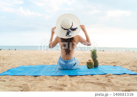Happy Asian woman sitting on beach mat enjoying summer vacation Happy Asian woman sitting on beach mat enjoying summer vacation 140081316