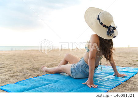 Back view of Asian woman sitting on beach mat looking at sea during summer holiday Back view of Asian woman sitting on beach mat looking at sea during summer holiday 140081321