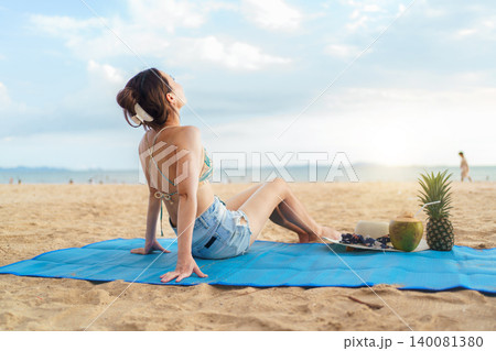 Asian woman relaxing on beach mat with tropical fruits at sunset 140081380