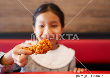 Cute Asian girl holding a piece of fried chicken in restaurant Cute Asian girl holding a piece of fried chicken in restaurant 140081400