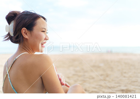 Asian woman applying sunscreen on shoulder at the beach Asian woman applying sunscreen on shoulder at the beach 140081421