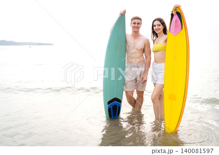 Young Couple Holding Surfboards Walking in the Sea at Beach Young Couple Holding Surfboards Walking in the Sea at Beach 140081597