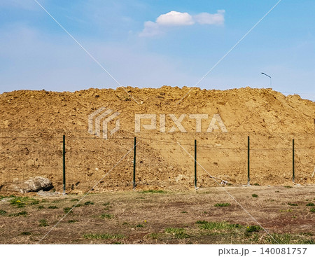 Outdoor construction earthworks with a large pile of sand behind the fence and a heavenly landscape 140081757