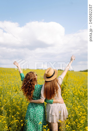 Two young happy women in middle of a yellow rapeseed field. Concept of fun, relaxation. Lifestyle. 140082287