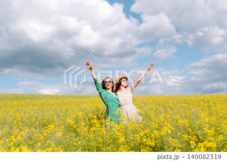 Two young happy women in middle of a yellow rapeseed field. Concept of fun, relaxation. Lifestyle. Two young happy women in middle of a yellow rapeseed field. Concept of fun, relaxation. Lifestyle. 140082319