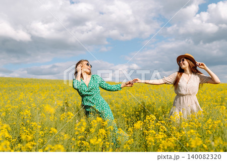 Two young happy women in middle of a yellow rapeseed field. Concept of fun, relaxation. Lifestyle. Two young happy women in middle of a yellow rapeseed field. Concept of fun, relaxation. Lifestyle. 140082320
