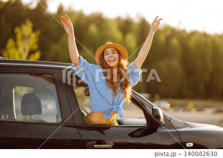 Smiling woman from the window of the car enjoys natureCar travel, sunset light. Active lifestyle. Smiling woman from the window of the car enjoys natureCar travel, sunset light. Active lifestyle. 140082630