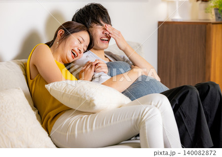 ソファーでテレビを見ながらくつろぐ若いカップル ソファーでテレビを見ながらくつろぐ若いカップル 140082872