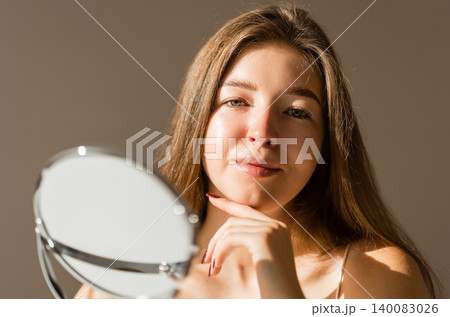 Young woman reflected in the mirror in soft evening light in a cozy room. Beauty and care concept. Young woman reflected in the mirror in soft evening light in a cozy room. Beauty and care concept. 140083026