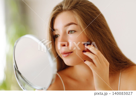 A beautiful woman looking in mirror, examines acne, pigmentation. Cosmetic care. Allergic reaction. A beautiful woman looking in mirror, examines acne, pigmentation. Cosmetic care. Allergic reaction. 140083027