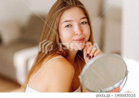A beautiful woman looking in mirror, examines acne, pigmentation. Cosmetic care. Allergic reaction. A beautiful woman looking in mirror, examines acne, pigmentation. Cosmetic care. Allergic reaction. 140083028