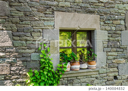 Stone window with flower pots on rustic house facade in Rupit village, Catalonia, Spain, featuring traditional masonry Stone window with flower pots on rustic house facade in Rupit village, Catalonia, Spain, featuring traditional masonry 140084832