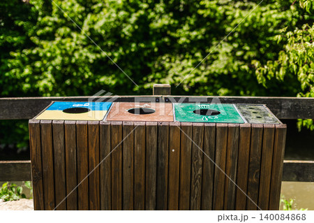 Wooden outdoor recycling station with separate waste sorting compartments in green park setting 140084868