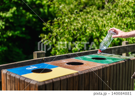 Person placing plastic bottle into recycling bin in public park, responsible waste sorting and recycling practice Person placing plastic bottle into recycling bin in public park, responsible waste sorting and recycling practice 140084881