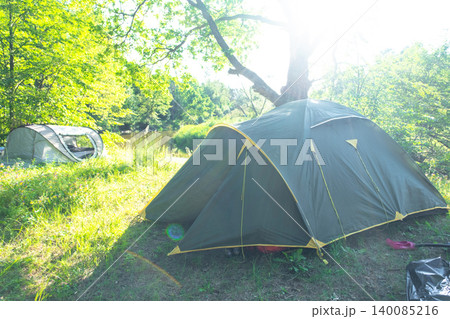 Classic dome tent in green summer clearing, sunlight filtering through trees, outdoor camping destination, tourism, back-to-nature travel experience. 140085216