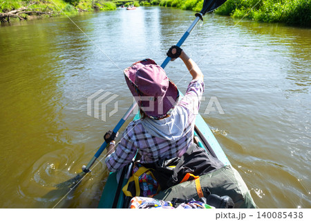 Woman in a kayak paddling on river, sporting hat, summer adventure, outdoor activity, nature tourism and water gear use. 140085438