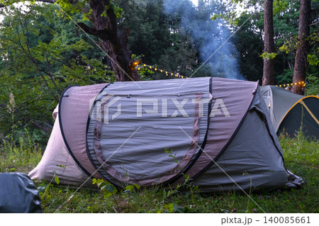 Outdoor camping tent with light smoke near trees, travel in nature, recreation and tourism, summer adventure setting, rural relaxation. Outdoor camping tent with light smoke near trees, travel in nature, recreation and tourism, summer adventure setting, rural relaxation. 140085661