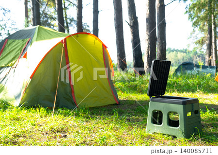 Portable camping toilet near yellow tent, outdoor facility, tourism convenience, field use for sanitation and comfort in nature area. 140085711